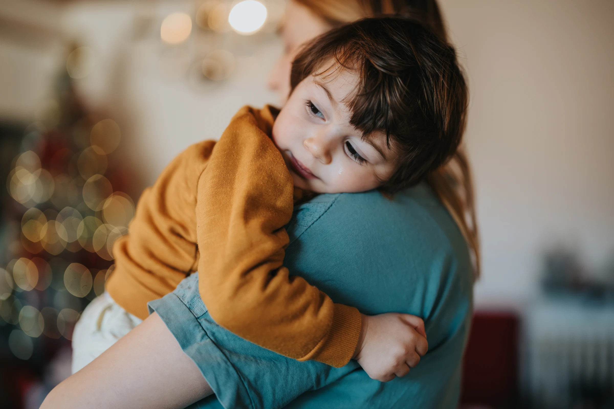A child rests their cheek on their mother’s shoulder.