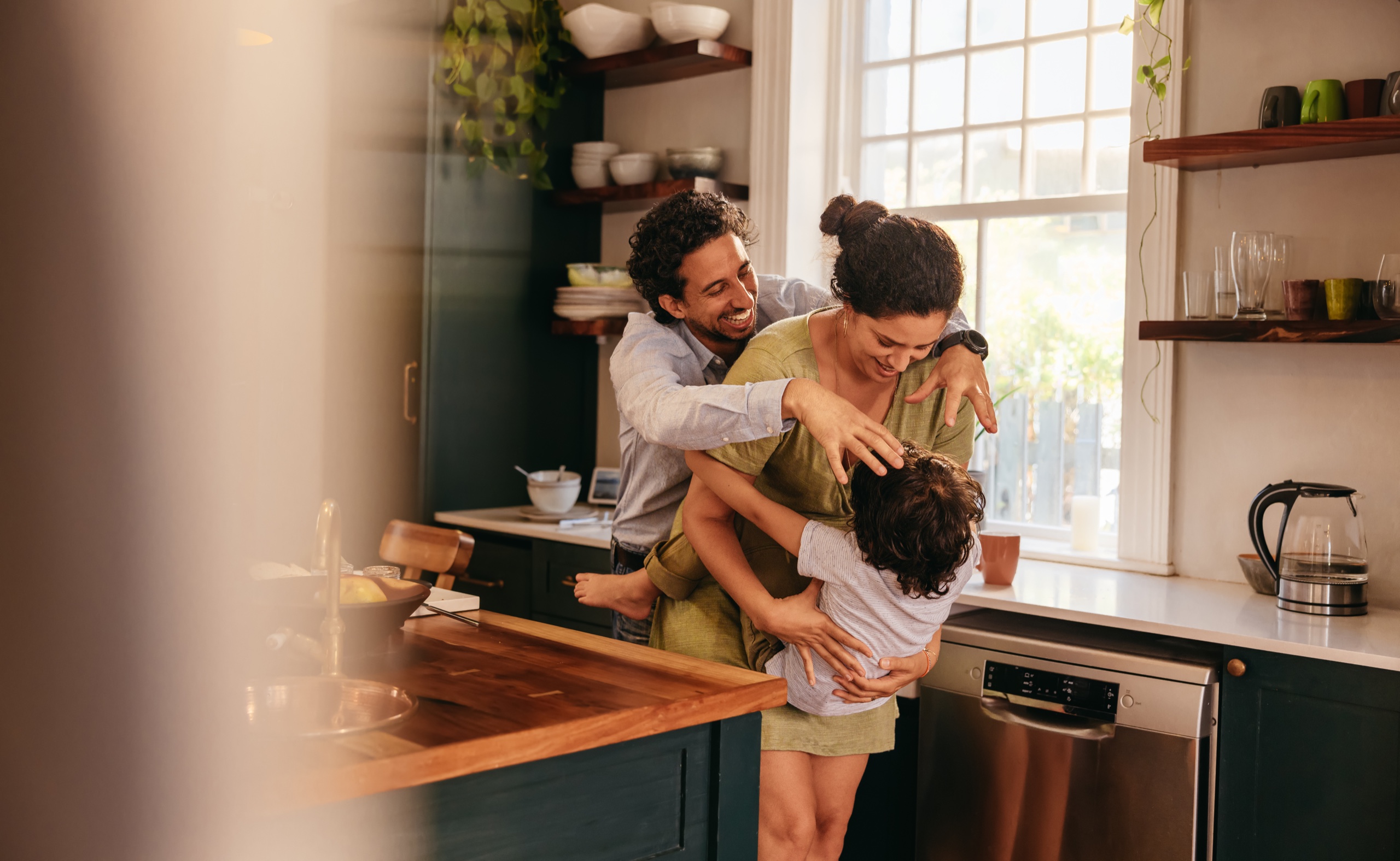 A family laughing and hugging together in a sunlit kitchen.
