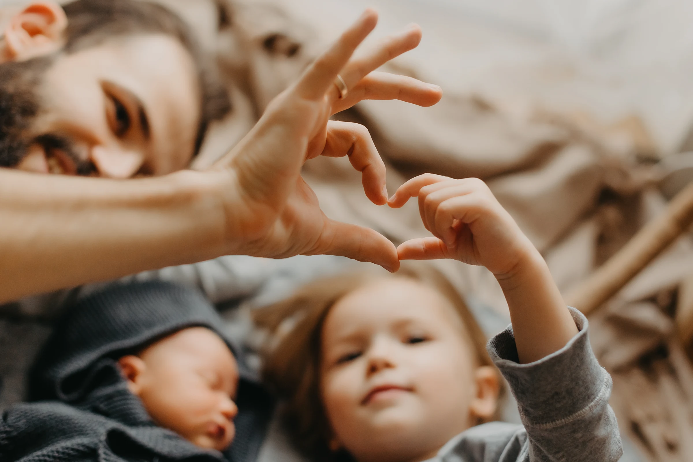 A family lies close together in bed, making a heart with their hands.