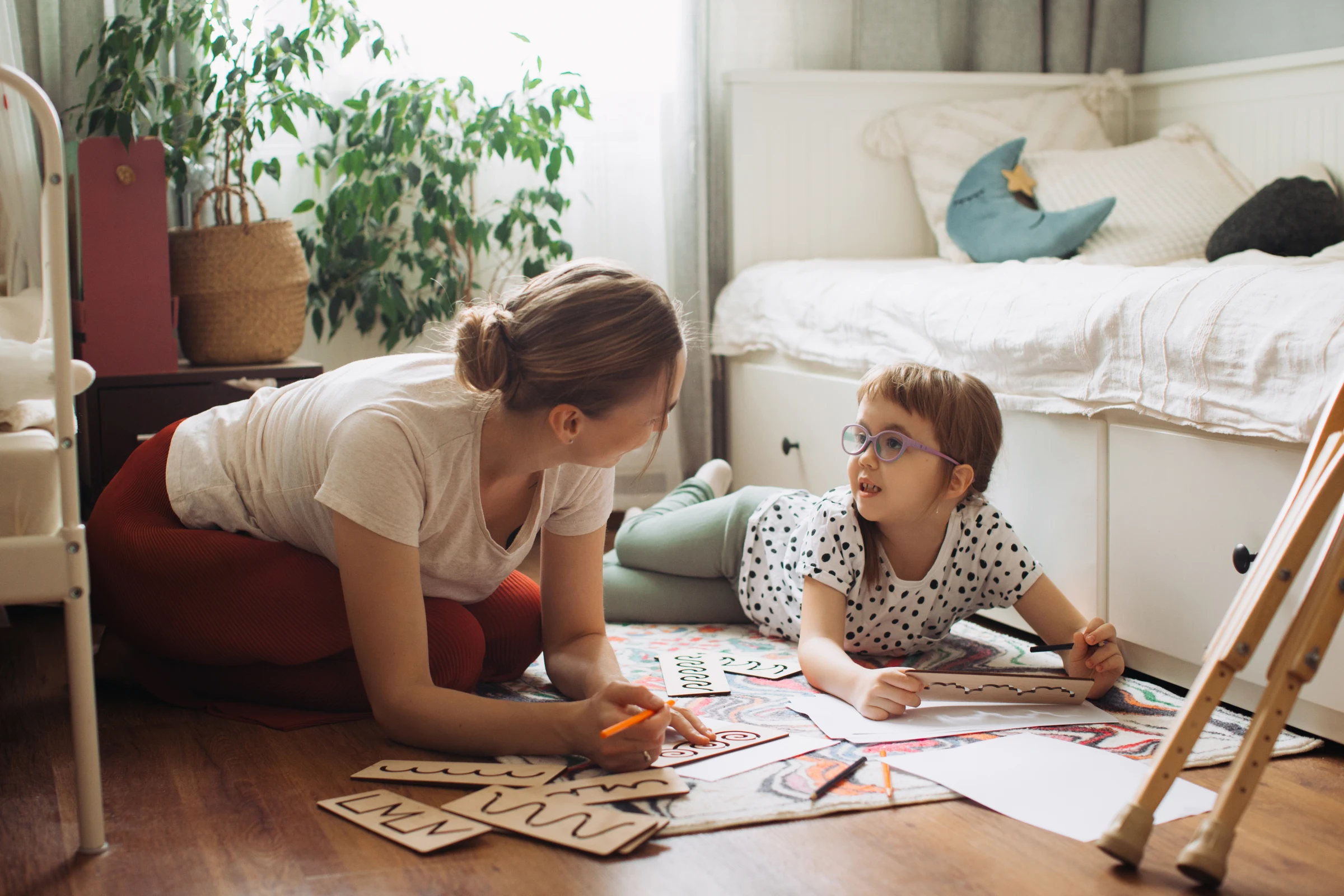 A mother and child draw together on the bedroom floor.